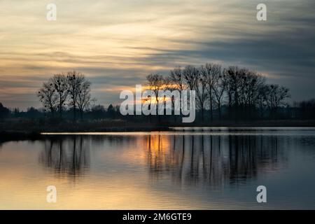 The sun behind the clouds and the reflection of trees in the water Stock Photo