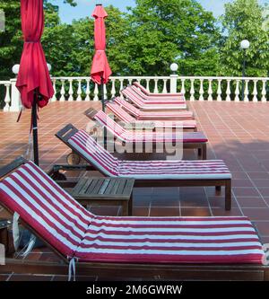 Empty wooden deck chairs with red and white striped mattresses stand in a row. Luxury outdoor recreation, sunshine Stock Photo