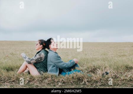 Couple in love in the field sitting back to back looking at the sky, Young relaxed couple sitting in the field with their backs to each other looking Stock Photo