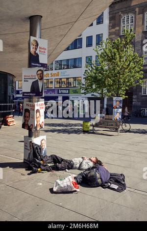 A man sleeps on the street outside Norreport Metro station in the sun, in Copenhagen, Denmark Stock Photo