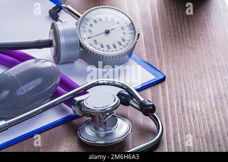 medical stethoscope blood pressure monitor on clipboard with blanc sheet of paper and vintage wooden board Stock Photo