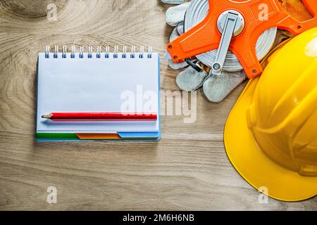 Notebook pencil protective gloves tape measure building helmet on wooden board. Stock Photo