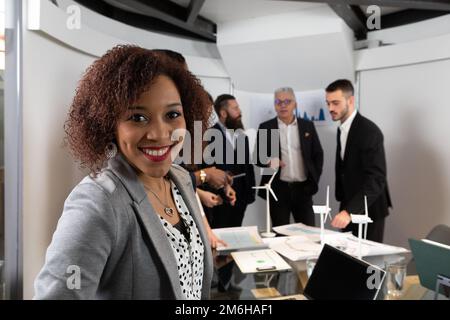 Portrait of a beautiful young African entrepreneur who looks in the camera, in the background colleagues at work. Starting of business, self -confiden Stock Photo