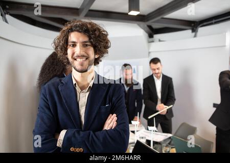 Young handsome businessman smiling in an office. Posed portrait with selective focus on the businessman and colleagues blurred in the background Stock Photo