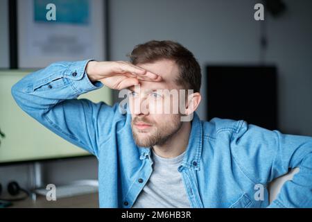 Cute bearded portrait of caucasian male freelance software engineer sitting at working place in office looking forward for new opportunities with computer on background. High quality image Stock Photo
