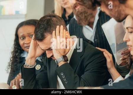 Desperate investor for the collapse of the markets surrounded by colleagues who console him. Hands in the hair and shocked expression for a strong los Stock Photo