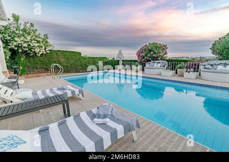 A pair of comfortable deck chairs surrounding a swimming pool during sunset along the Costa Del Sol close up Stock Photo