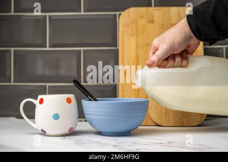 man pouring vegan oat soya almond or  coconut milk onto breakfast cereals in kitchen Stock Photo