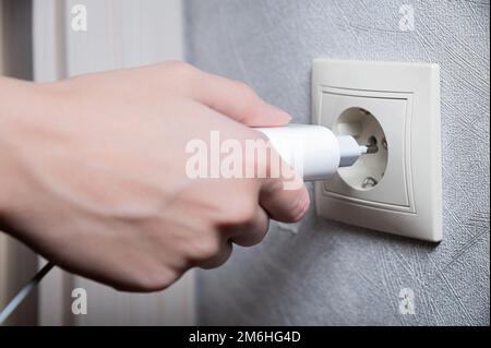 Close-up of a woman's hand inserting a white usb charger into a 220 volt socket Stock Photo