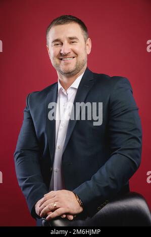 Handsome caucasian joyful businessman standing in the studio on a red background smiling looking at the camera. Studio portrait Stock Photo