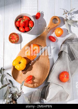 Assorted tomatoes on a kitchen wooden board. Colorful tomatoes of different varieties and colors. Organic and fresh vegetables from the garden. Top vi Stock Photo