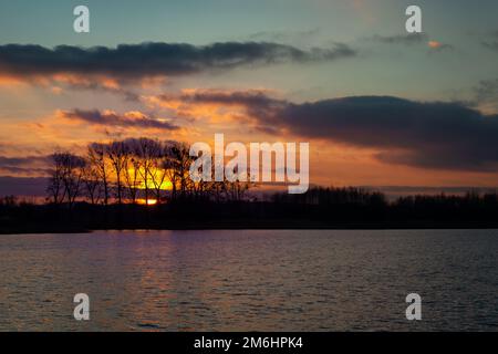 Sunset and clouds behind the trees on the lake Stock Photo