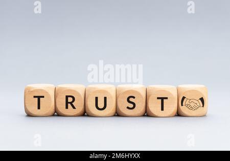 Trust concept. Text and handshake icon on wooden blocks on gray background. Copy space Stock Photo