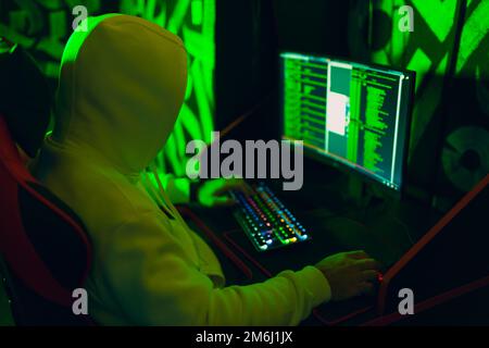 Hacker in hoodie working hacks code site on personal computer with green light Stock Photo