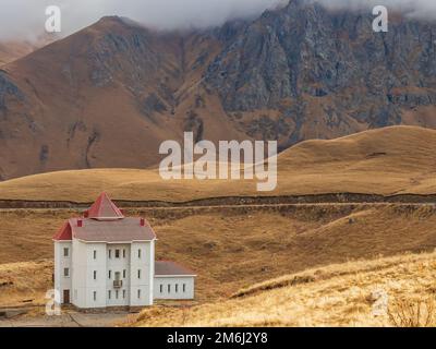 High in the autumn mountains of the Caucasus, where the clouds lie on the peaks, there is a white house with narrow windows and Stock Photo