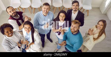 Multiethnic team of happy young business people standing in office, smiling and applauding Stock Photo