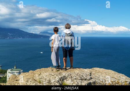 Grandmother and grandson are standing on the edge of a cliff high above the sea. Stock Photo