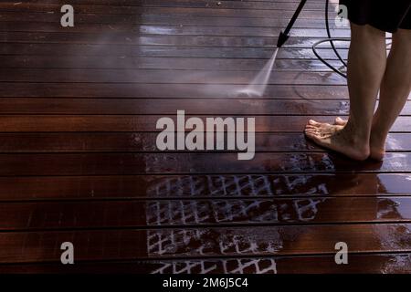 Power surface washing. Man cleaning terrace with a power washer. High water pressure cleaner on wooden terrace surface. Stock Photo