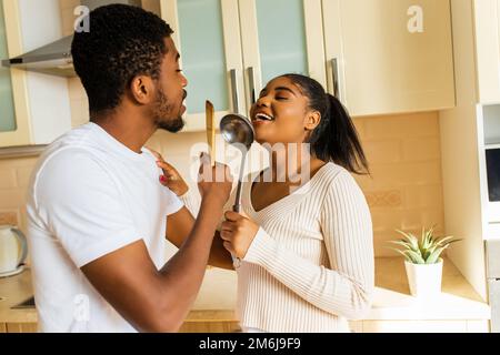 hispanic couple singing together holding a ladle like a microphone in the kitchen Stock Photo