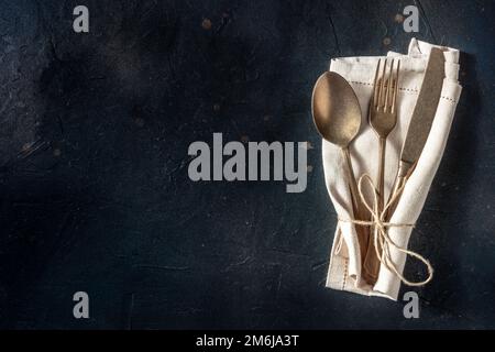 Cutlery. A spoon, a fork, and a knife in a napkin on a black background Stock Photo