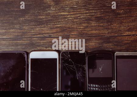 An assortment of outdated and damaged mobile phones with broken screens ready for repair on a wooden background with copy space Stock Photo
