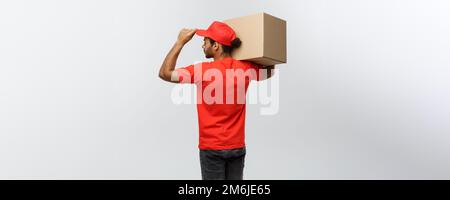 Delivery Concept - back view of Handsome African American delivery man with box package. Isolated on Grey studio Background. Cop Stock Photo