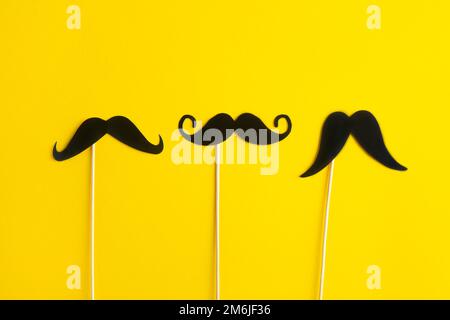 Father's Day Holiday Concept. Transparent glasses, stylish black paper photo booth props moustaches on yellow background. Stock Photo
