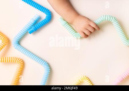 Trendy kids toys pastel colorful pop-tube in baby toddler hands on beige background. Set of forms and colors corrugated pipe and Stock Photo