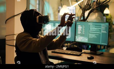 Male cyber criminal hacking network system with vr headset, using virtual reality to steal passwords and info illegally. Young adult using hacktivism skills to break into security server. Stock Photo