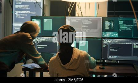Diverse criminals hacking security server with malware, working on cyberbullying late at night. Hackers phishing for information, stealing valuable data, breaking firewall encryption. Stock Photo
