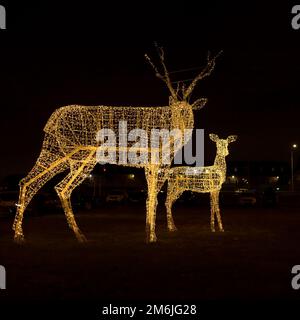 Two luminous deer figurines stand on the night lawn. Christmas decoration of the city Stock Photo