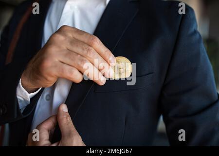 Male ceo manager in suit putting bitcoin coin in pocket, standing in office interior, closeup, cropped Stock Photo