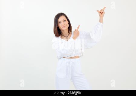 Portrait of young woman standing, raising hands, pointing with index fingers, looking at camera on white background. Stock Photo