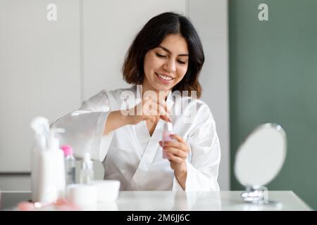 Smiling pretty young woman using face serum at home Stock Photo