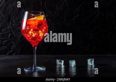 Aperol cocktail with a fresh orange and ice cubes, a side view on black Stock Photo