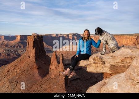 Portrait of cheerful woman sitting with dog on rock in desert Stock Photo