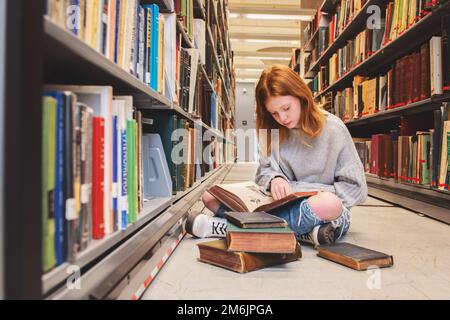 Teen Redhead Girl Sitting With Pile of Books in Library Stock Photo - Alamy