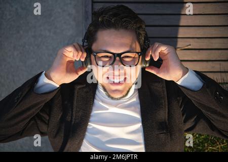 Asian guy in glasses and headphones, resting lying on a wooden bench Stock Photo