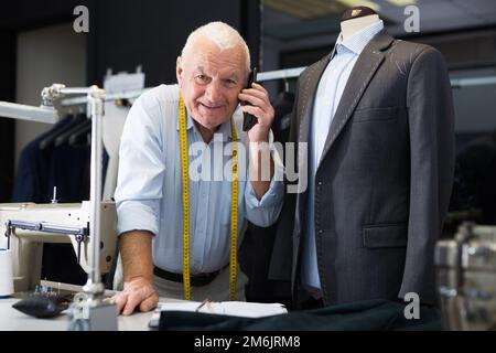 Professional tailor communicates with the client on mobile phone and takes notes in notebook Stock Photo