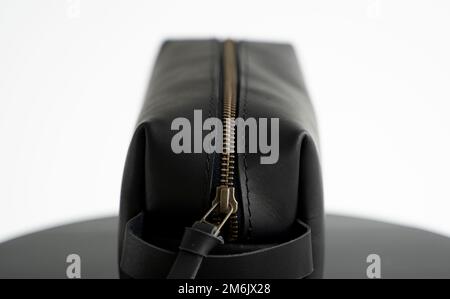 Close up black leather classic mens cosmetic bag with a metal gold zip on a black chair with a white background. Stock Photo