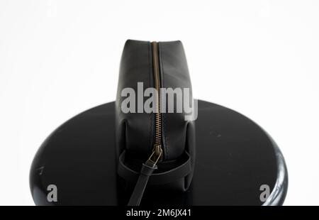 Black leather classic mens cosmetic bag with a metal gold zip on a black chair with a white background. Stock Photo