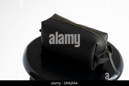 Side view black leather classic mens cosmetic bag with a metal gold zip on a black chair with a white background. Stock Photo