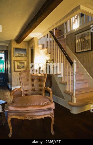 Antique wooden grid high back chair and carpeted staircase in living room inside old 1809 cottage style home. Stock Photo