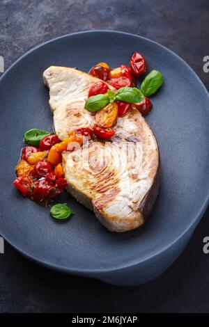 Fried swordfish steak with tomatoes and paprika served as close-up on a design plate Stock Photo