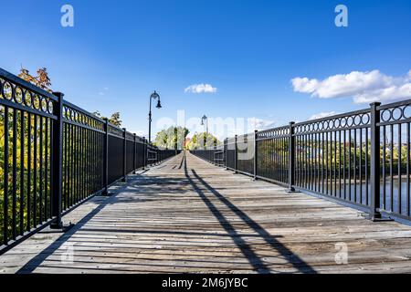 Colorful atmospheric autumn landscape with pedestrian bridge across the river and Maple trees on the river banks at sunlight in  Manchester New Hampsh Stock Photo