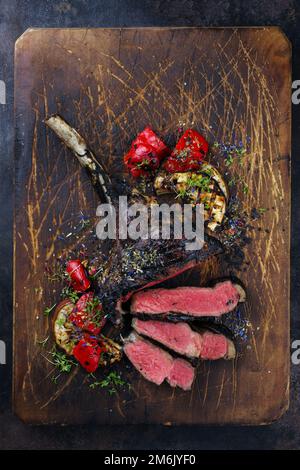 Modern style barbecue dry aged angus tomahawk steak with grilled vegetable served as top view on an old rustic wooden board Stock Photo
