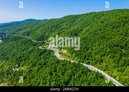 Winding road is meandering between blue sea and green mountains. Aerial view of car driving along the winding mountain road in S Stock Photo