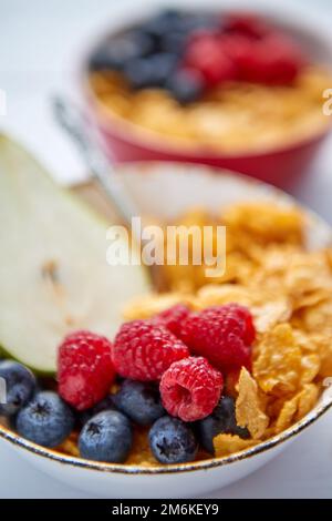 Golden cornflakes with fresh fruits of raspberries, blueberries and pear in ceramic bowl Stock Photo