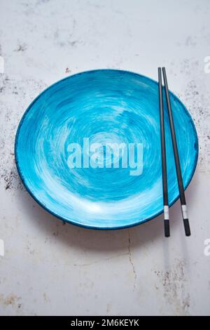 Turquoise hand painted ceramic serving plate with wooden chopsticks on side Stock Photo
