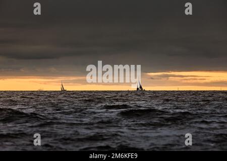 Sailboat in sea at stormy weather, stormy clouds sky orange sky, sail regatta, reflection of sail in the water, bigl waves of wa Stock Photo